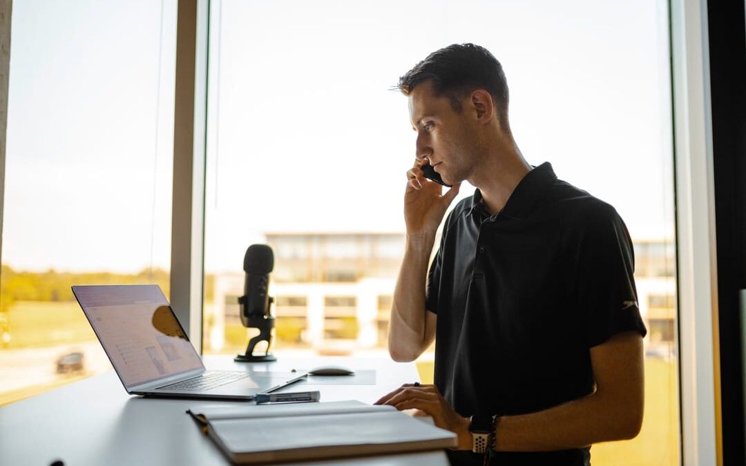 man standing in front of office window at desk, on phone