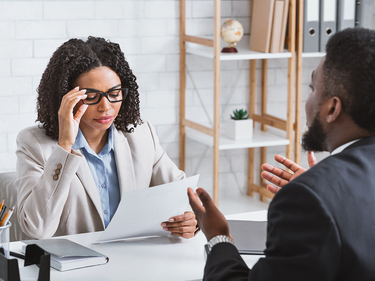 Female human resources manager reading vacancy applicant's resume during job interview at office